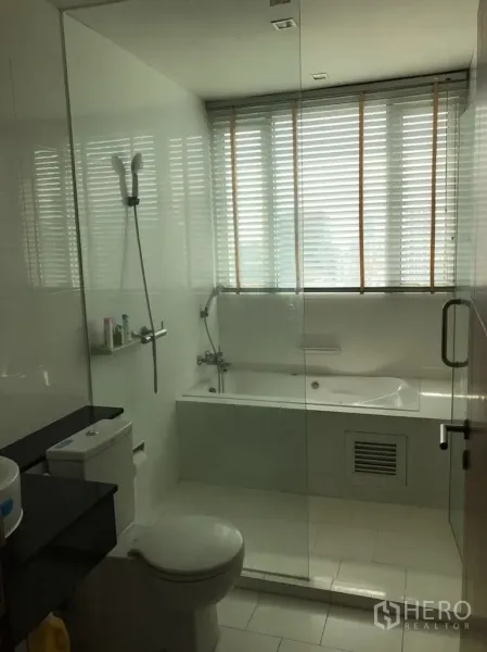 Condominium for rent in Watthana, Bangkok - Modern bathroom with glass partition, bathtub under a window with blinds, shower, toilet and vanity.