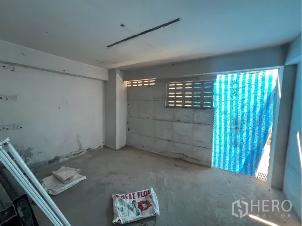 Shophouse for rent in Bangkok - Rear room with cement floor, ventilation block windows and a blue temporary sheeted doorway.