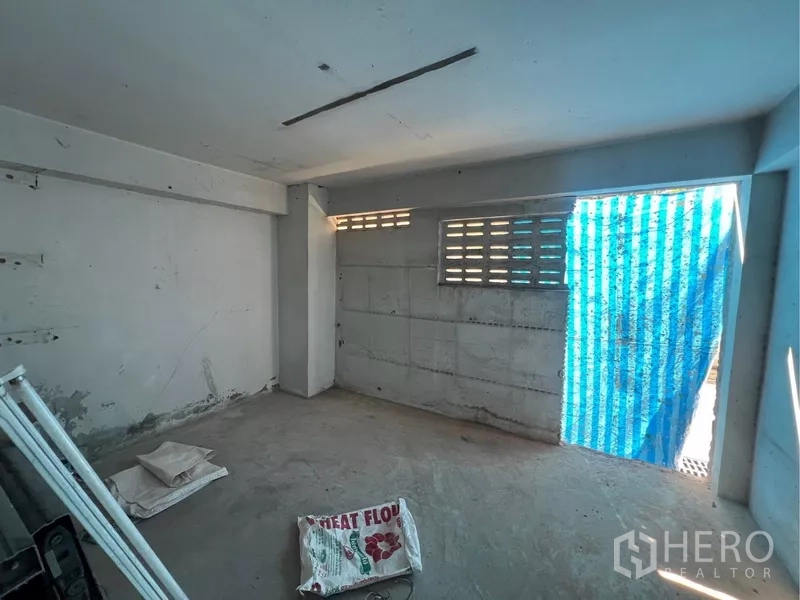 Shophouse for rent in Bangkok - Rear room with cement floor, ventilation block windows and a blue temporary sheeted doorway.