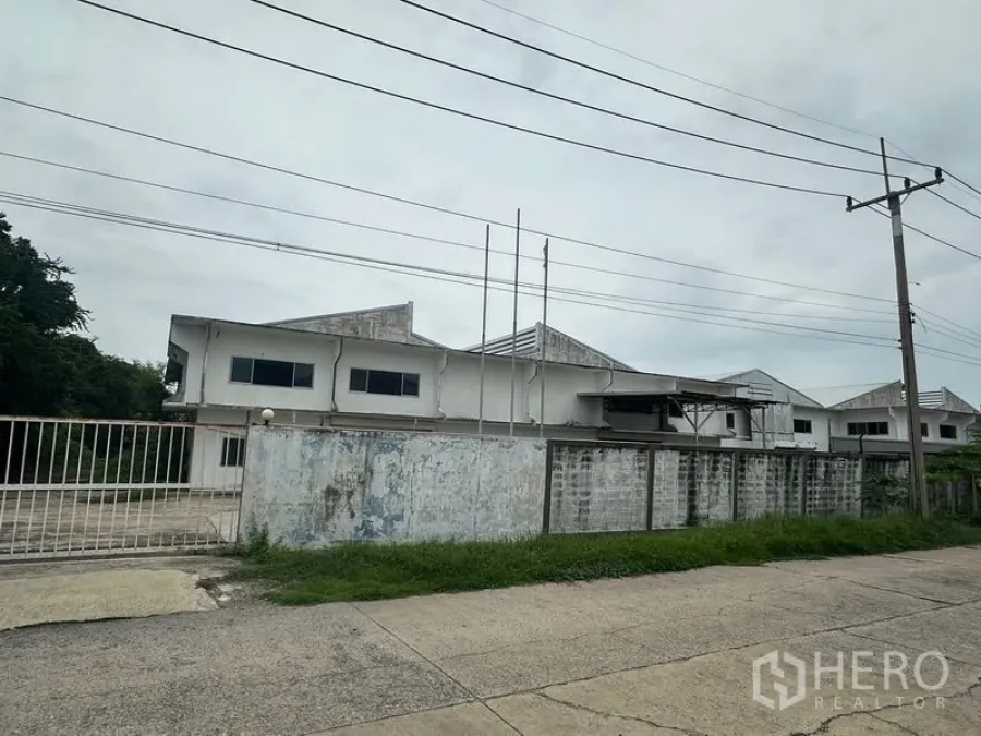 Factory for rent or sale in Khlong Luang, Pathum Thani - Streetside view of a gated standalone factory complex with perimeter wall and power lines in Khlong Luang.