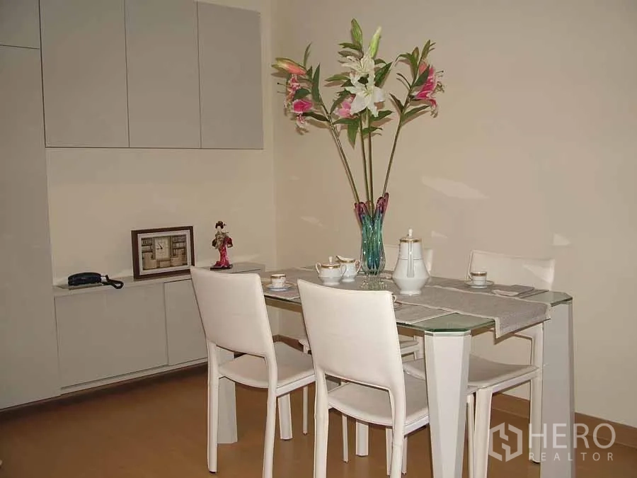 Condominium for rent or sale in Watthana, Bangkok - Dining corner featuring a glass-top table with four white chairs and built-in storage cabinets.