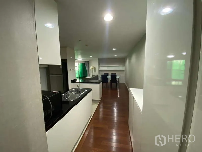 Condominium for  in Huai Khwang, Bangkok - Kitchen corridor leading to dining area with wood flooring and ample cabinet storage.