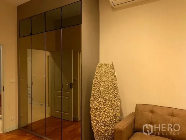 Detached House for rent or sale in Khan Na Yao, Bangkok - Room corner with mirrored built-in wardrobe, beige sofa and sculptural floor lamp.