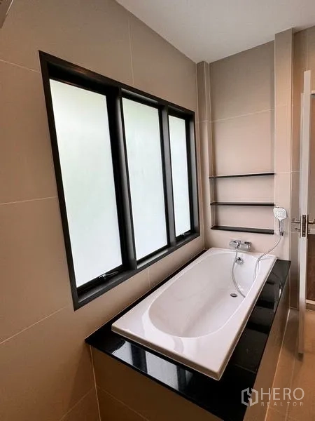 Detached House for rent or sale - Bathroom with built-in bathtub below frosted windows and wall shelves.