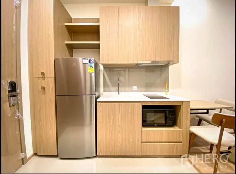 Condominium for sale in Chatuchak, Bangkok - Compact built-in kitchen with wood cabinets, fridge, cooktop and dining nook.