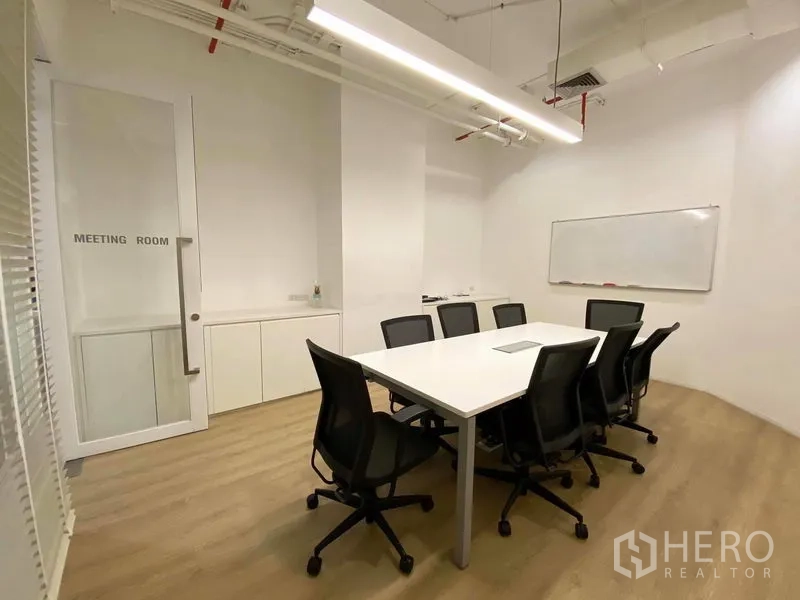 Office Space for rent in Bangkok - Enclosed meeting room with a rectangular table, eight chairs, whiteboard and linear pendant lighting.