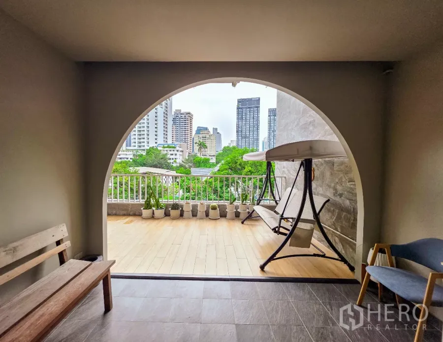 อาคารพาณิชย์ ให้เช่าในWatthana, Bangkok - ระเบียงซุ้มโค้งมองเห็นสกายไลน์เมืองและแนวต้นไม้ พร้อมชิงช้าแบบเบาะยาว