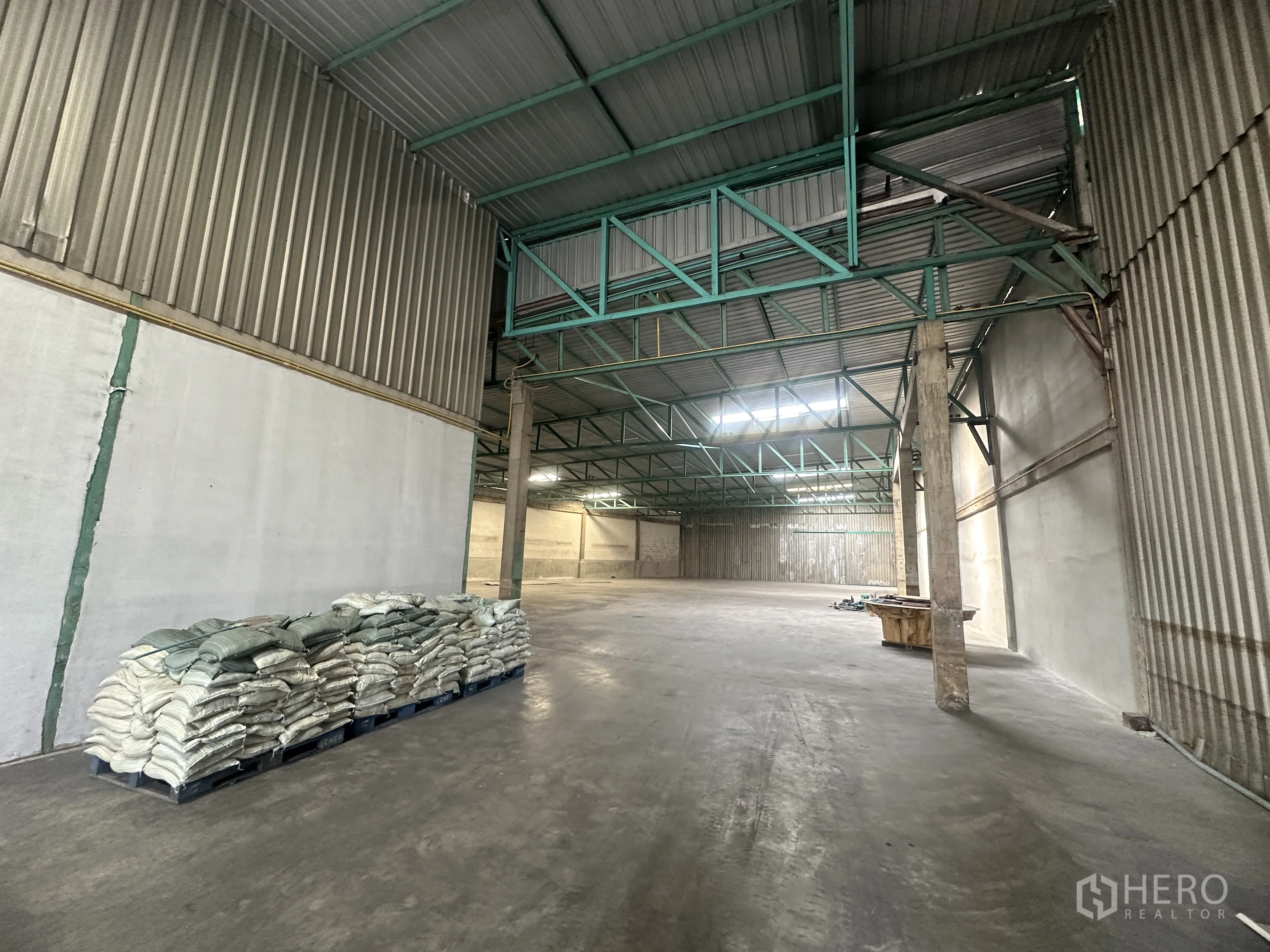 货栈 出租在Mueang Pathum Thani, Pathum Thani - 仓库装卸与存储区，混凝土立柱、镀锌板墙面，托盘袋装物料。