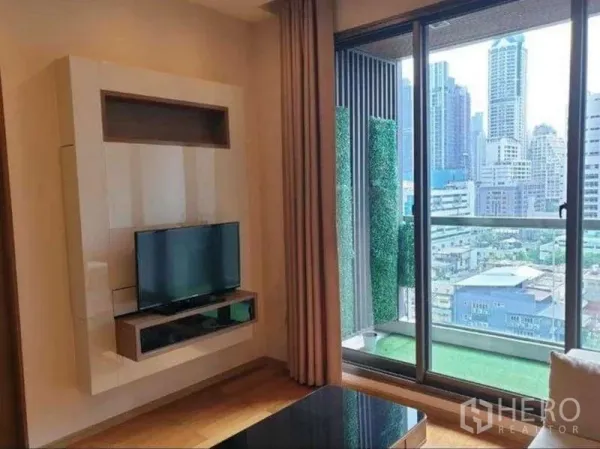 Condominium for rent in Bang Rak, Bangkok - Media wall with TV facing a balcony with artificial turf and expansive city view from a high floor.