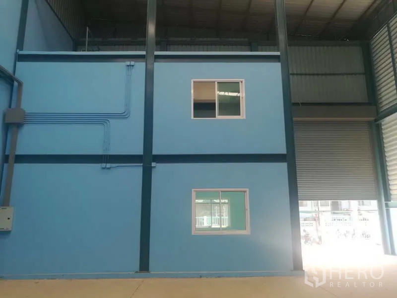工厂 出售在Sai Noi, Nonthaburi - 仓内两层办公室盒体，外露电管与卷闸门一并可见。