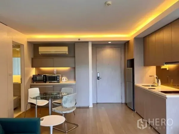 Condominium for rent in Watthana, Bangkok - Modern kitchenette with built-in cabinets, glass dining table, and soft LED lighting.