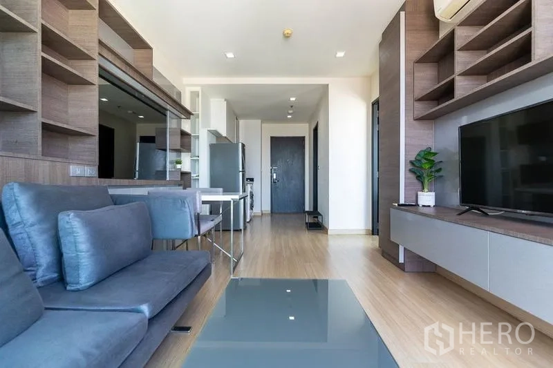 Condominium for rent - Open-plan living room facing TV wall and entry door with warm wood flooring.