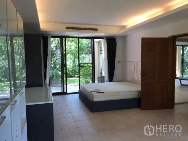 Detached House for rent in Watthana, Bangkok - Ground-floor bedroom opening to the garden through sliding doors, with tiled floor and storage cabinets.