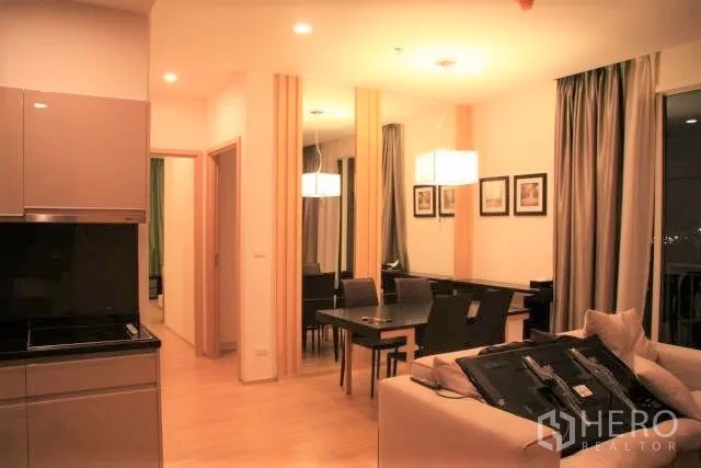 Condominium for rent in Watthana, Bangkok - Dining area with mirrored feature wall, pendant lights and large curtains next to the kitchen.