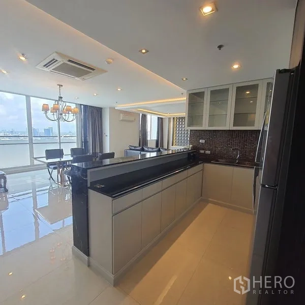 Condominium for rent in Bang Kapi, Bangkok - Open-plan kitchen with long black countertop, dining area and floor-to-ceiling windows overlooking Bangkok’s skyline.