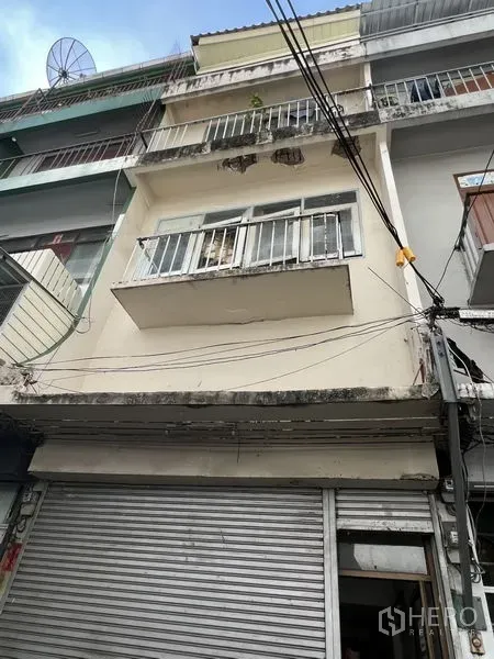 店屋 出租在Watthana, Bangkok - 临街多层店屋外立面，带阳台与金属卷闸门，仰视视角。