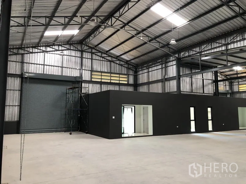 工厂 出租在Bang Yai, Nonthaburi - 室内空间，卷闸装卸门与灰色办公室位于高屋顶下。