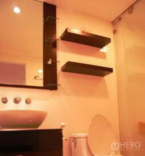 公寓 出租在Pathum Wan, Bangkok - 现代浴室，台上盆、墙面置物架、坐便器与玻璃淋浴间。