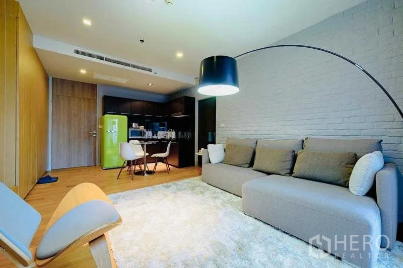 Condominium for rent in Watthana, Bangkok - Open‑plan living with sofa, dining set and kitchenette with bright green fridge.