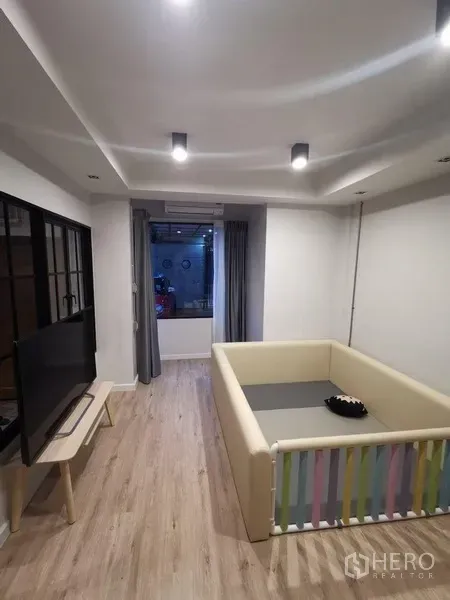 Townhouse for rent in Din Daeng, Bangkok - Modern living room with recessed lights, TV console and a children’s play area on light wood floors.