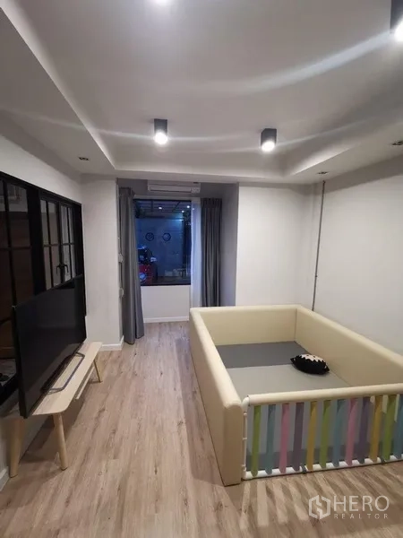 Townhouse for rent in Din Daeng, Bangkok - Modern living room with recessed lights, TV console and a children’s play area on light wood floors.