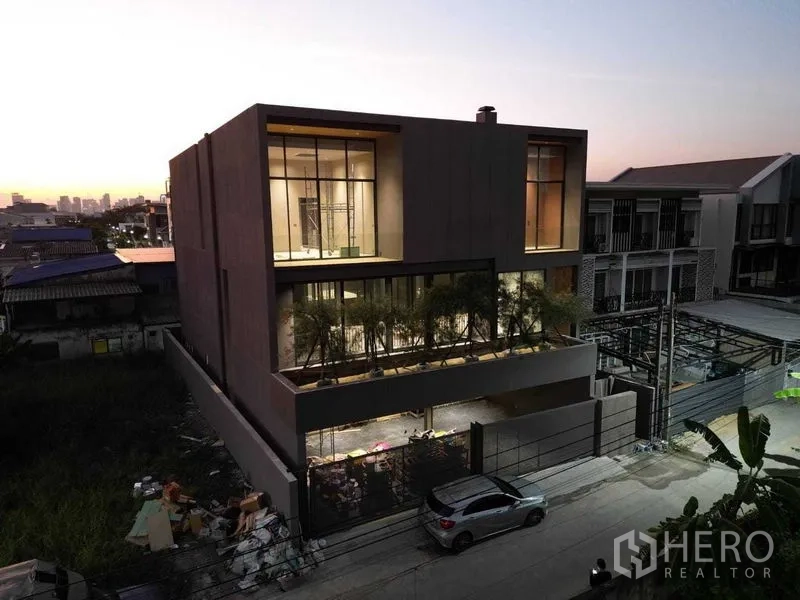 独立式住宅 出售在Lat Phrao, Bangkok - 当代独栋立面，带入户车道与大面积玻璃，傍晚灯光。