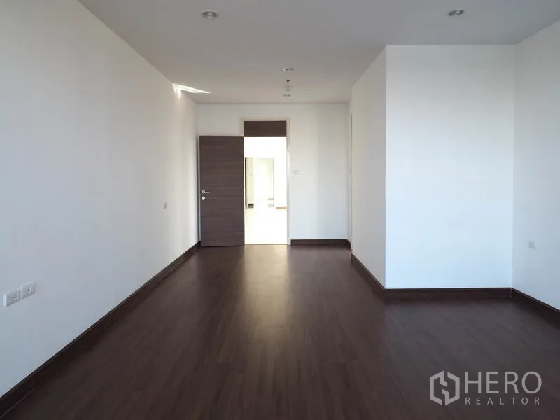 Condominium for rent in Yan Nawa, Bangkok - Spacious bedroom with wood floors, white walls and an open doorway to the hall.
