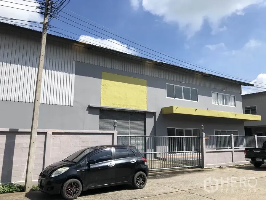 工厂 出租在Pathum Thani - Lat Lum Kaeo两层工厂外立面，灰墙配黄色雨棚，金属大门与停车位。