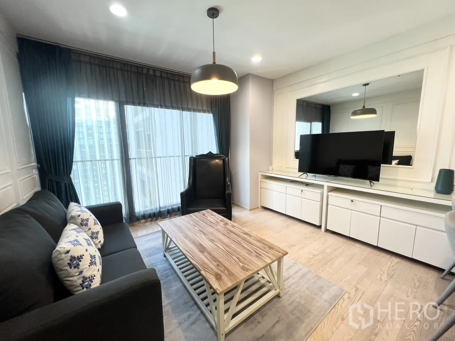 คอนโด for rent in Khlong Toei, Bangkok - ห้องนั่งเล่นสว่าง โปร่ง ด้วยโซฟา เก้าอี้วิงแบ็ก โต๊ะกลางไม้ ตู้วางทีวีบิลต์อิน และกระจกเต็มบานมองเห็นวิวเมือง