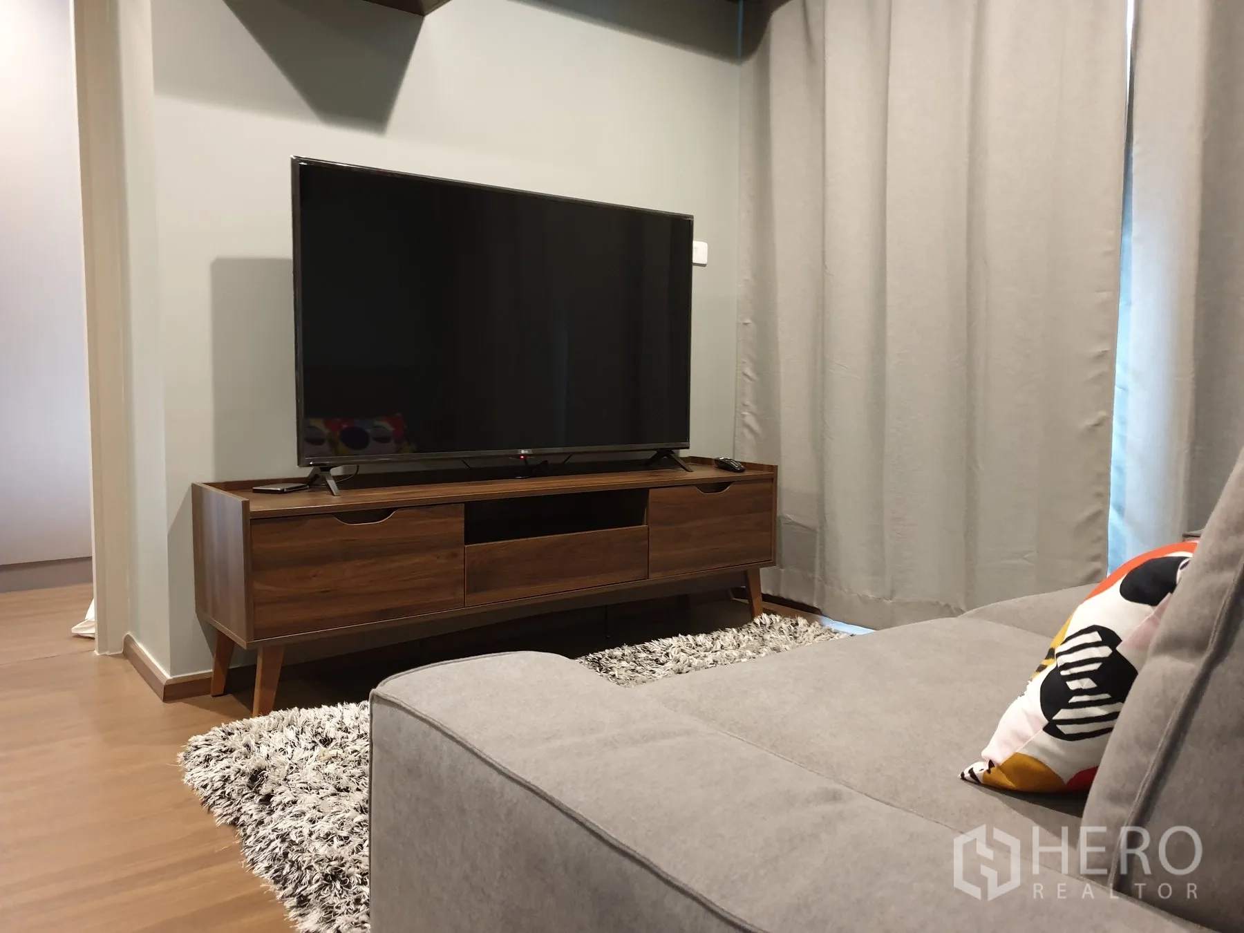 คอนโด for rent in Phra Khanong, Bangkok - ห้องนั่งเล่นโซฟาสีเทา ชั้นวางทีวีไม้ และผ้าม่านเต็มบาน