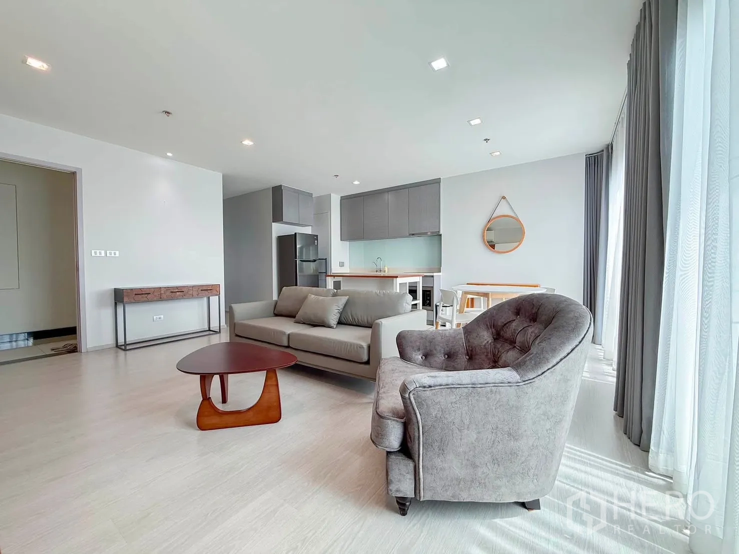 Condominium for rent in Khlong Toei, Bangkok - Bright living space with sofa set, armchair, and large curtained windows.