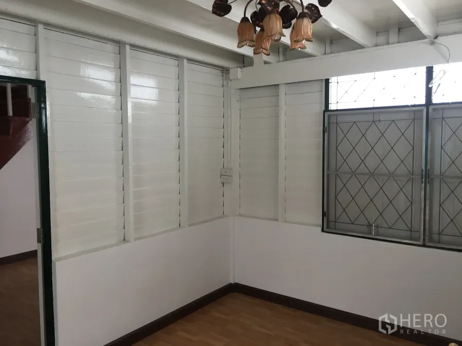 Detached House for rent in Bang Rak, Bangkok - Bright living area with white louvered wall panels, wood flooring, a grilled window and a pendant light.