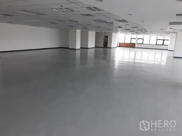 Office Space for rent in Bangkok - Spacious open-plan office floor with polished gray flooring, white columns, and a suspended ceiling with lighting.
