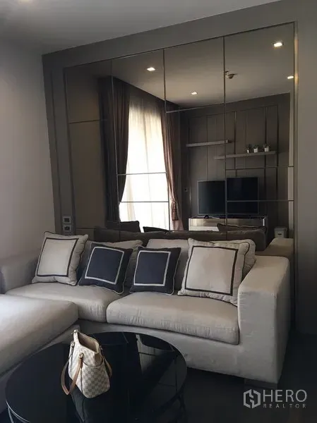 Condominium for rent in Watthana, Bangkok - Cozy lounge featuring plush sofa, large mirrored feature wall reflecting TV console and natural light.