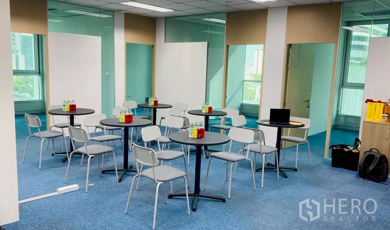 Office Space for rent in Sathon, Bangkok - Open-plan workspace with round tables, chairs, blue carpet and glass partitions.