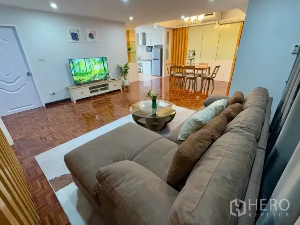 Condominium for rent in Huai Khwang, Bangkok - View from the sofa to a TV console and open dining area with warm parquet floors and indoor plant accents.