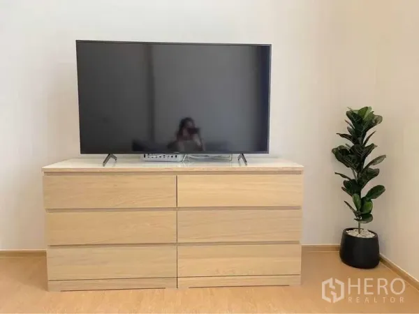 Condominium for rent in Watthana, Bangkok - Flat-screen TV on a light wood dresser with a potted plant in a minimalist living area.