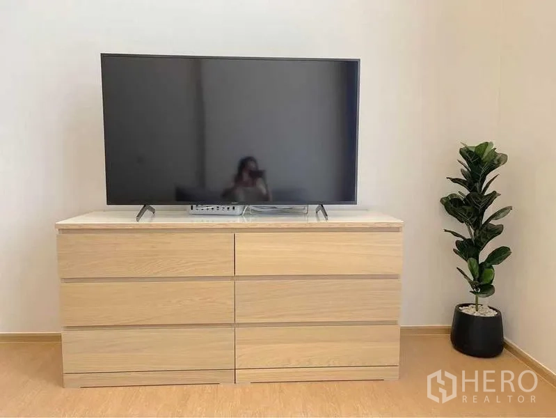 Condominium for rent in Watthana, Bangkok - Flat-screen TV on a light wood dresser with a potted plant in a minimalist living area.