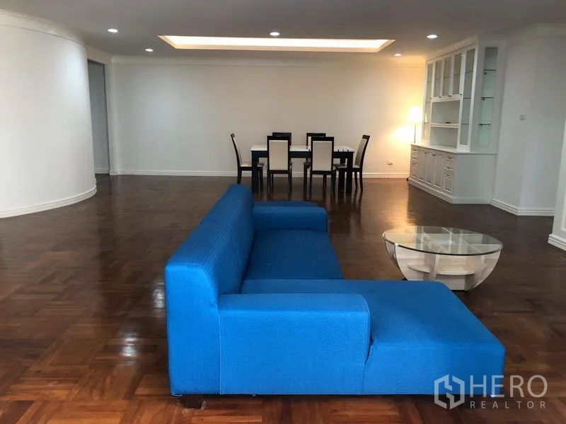 Condominium for rent in Watthana, Bangkok - Open-plan living and dining area with blue sofa, glass coffee table, six-seat dining set and cove lighting.