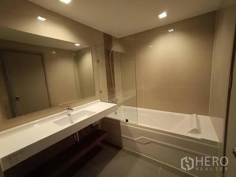 公寓 出租在Phra Khanong, Bangkok - 现代浴室，超长洗手台与大镜子，浴缸配玻璃隔断。