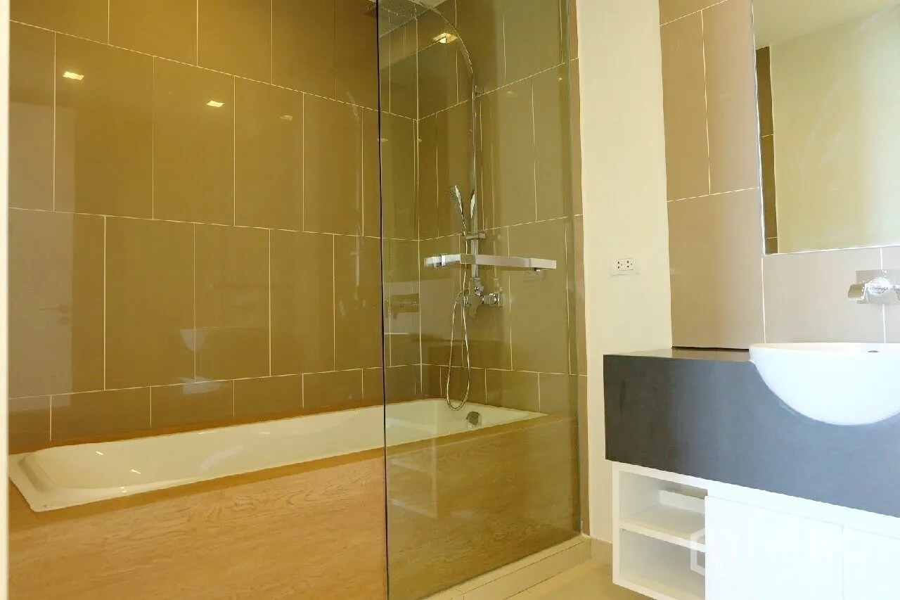 Condominium for rent or sale in Bang Lamung, Chon Buri - Modern bathroom with bathtub, glass shower screen, tiled walls and a sleek vanity.