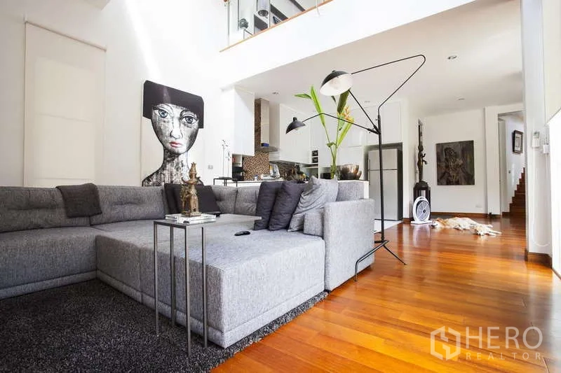 独立式住宅 出租在Lat Phrao, Bangkok - 灰色转角沙发的客厅，挑高空间连接现代厨房。