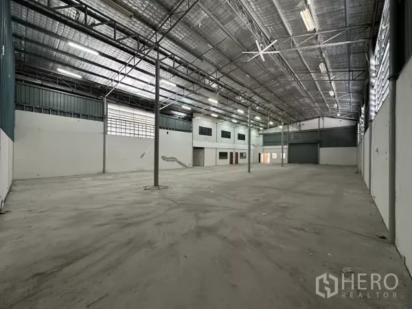 Warehouse for rent in Suan Luang, Bangkok - Wide industrial storage hall with smooth concrete slab, multiple support columns, and a large roller shutter door.