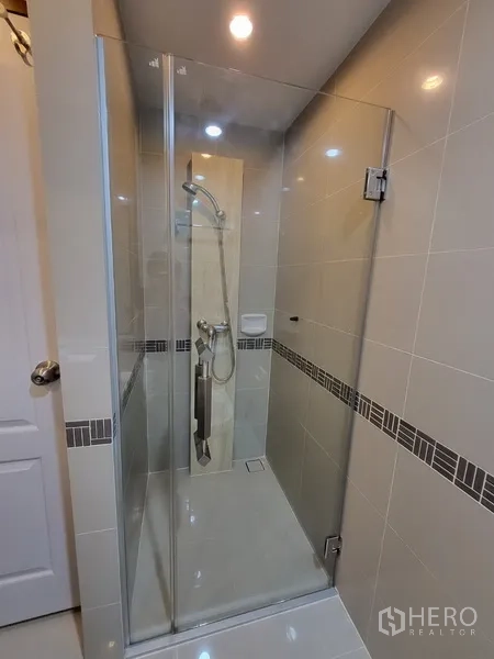 Condominium for rent in Phra Khanong, Bangkok - Glass-enclosed shower with handheld showerhead and neutral tiles.