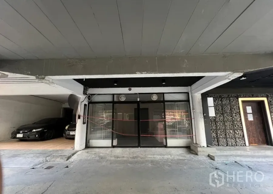 店屋 出租在Watthana, Bangkok - 一层店屋外立面，黑框玻璃门，前方为有顶停车区。