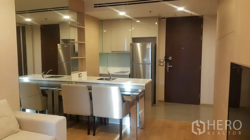 公寓 出租在Ratchathewi, Bangkok - 开放式厨房，带就餐中岛、亮面橱柜与不锈钢冰箱，紧邻入户门。