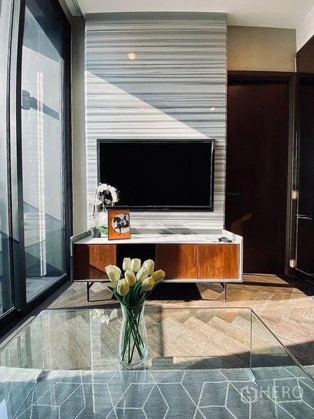 Condominium for rent in Khlong Toei, Bangkok - TV console on marble-patterned feature wall with natural light streaming through tall windows.