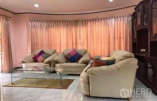 Detached House for rent in Khlong Sam Wa, Bangkok - Bright living room with beige leather sofas, glass coffee table, tiled floors and full-length curtains in a detached house.