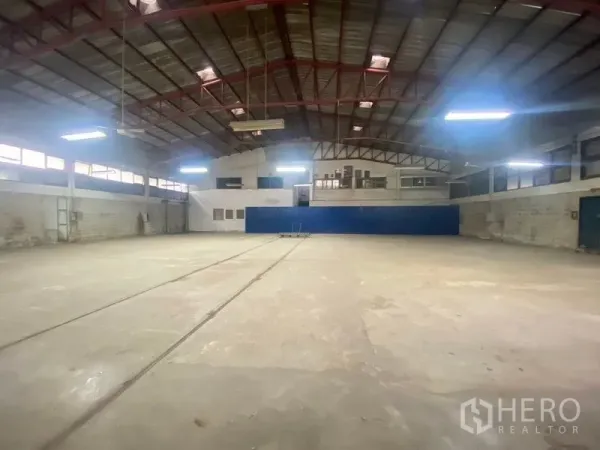 Warehouse for rent or sale in Suan Luang, Bangkok - Open warehouse interior with high steel truss roof, bright fluorescent lighting and mezzanine office windows.