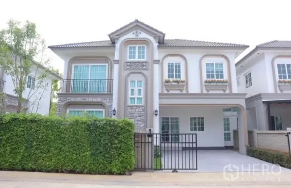 Detached House for rent in Bang Phli, Samut Prakan - Front exterior of two-storey house showing carport, balcony and landscaped hedge.